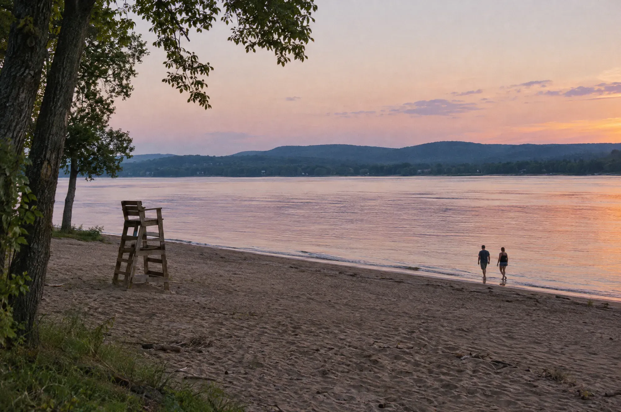 A small sandy beach on the Ottawa River at dusk, with low blue hills on the far shore and two people at the waterline.